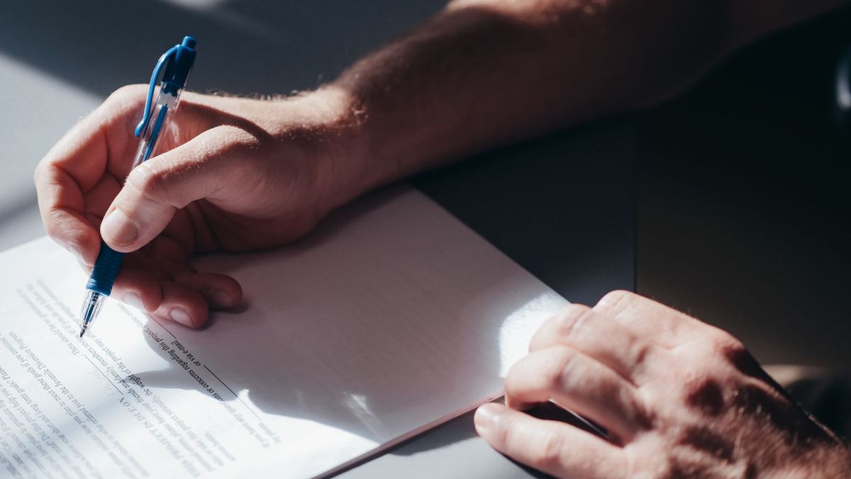 A hand signing a paper document with a blue pen